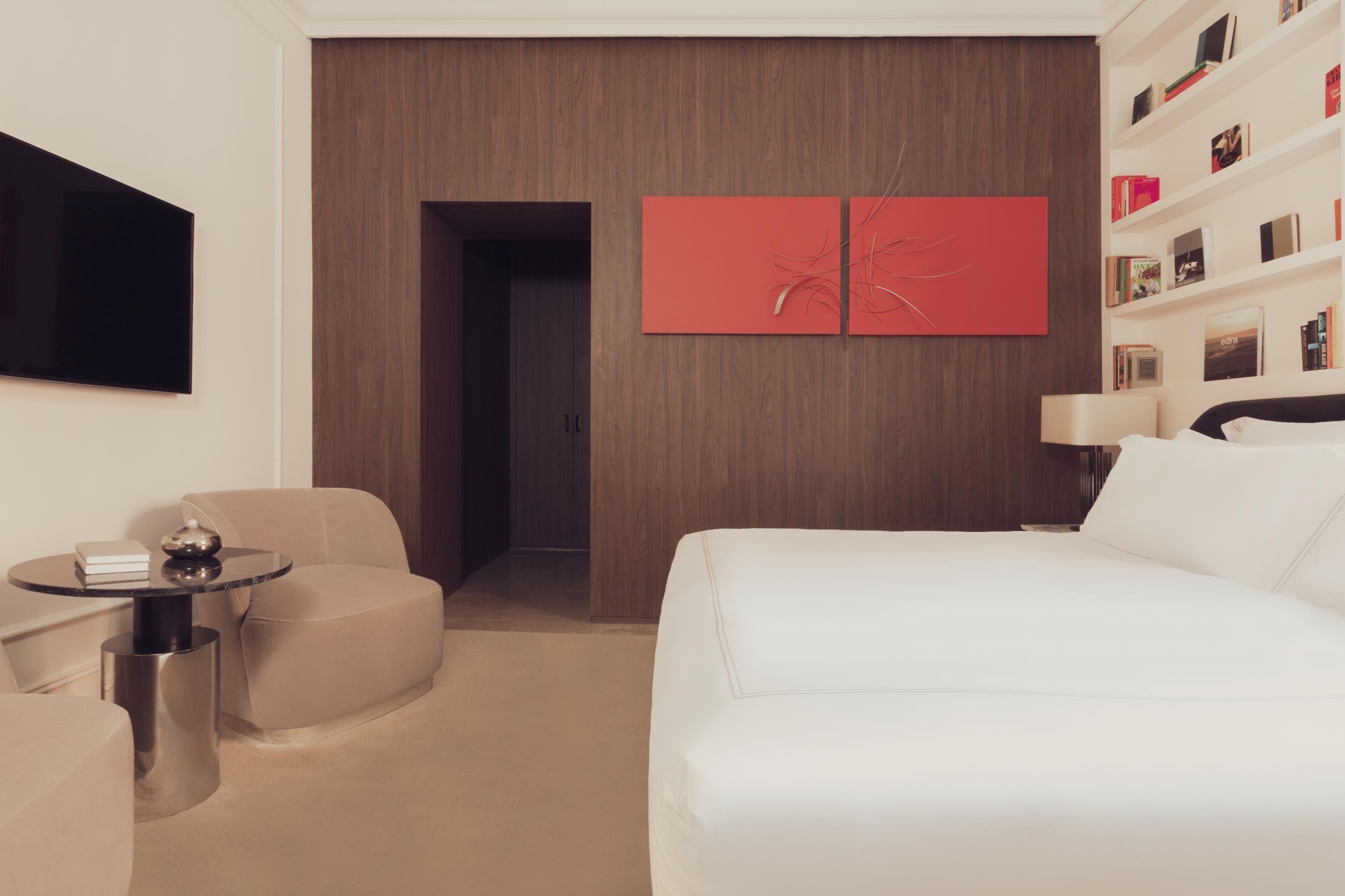 Ein modernes Hotelzimmer mit einem Bett, einem runden Tisch mit Lampe, einer Couch und einem an der Wand befestigten Fernseher.