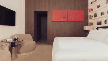 Ein modernes Hotelzimmer mit einem Bett, einem runden Tisch mit Lampe, einer Couch und einem an der Wand befestigten Fernseher.