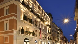 Un hôtel à plusieurs étages doté de balcons, situé sur une rue et dont l’enseigne est illuminée.
