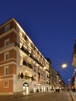 Un hotel de varios pisos con balcones, una calle delante y señalización iluminada.