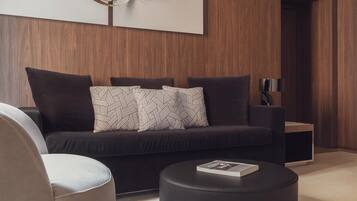 Un salon moderne avec un canapé de couleur foncée, des coussins à motifs, un pouf rond noir et une table d’appoint avec une lampe.