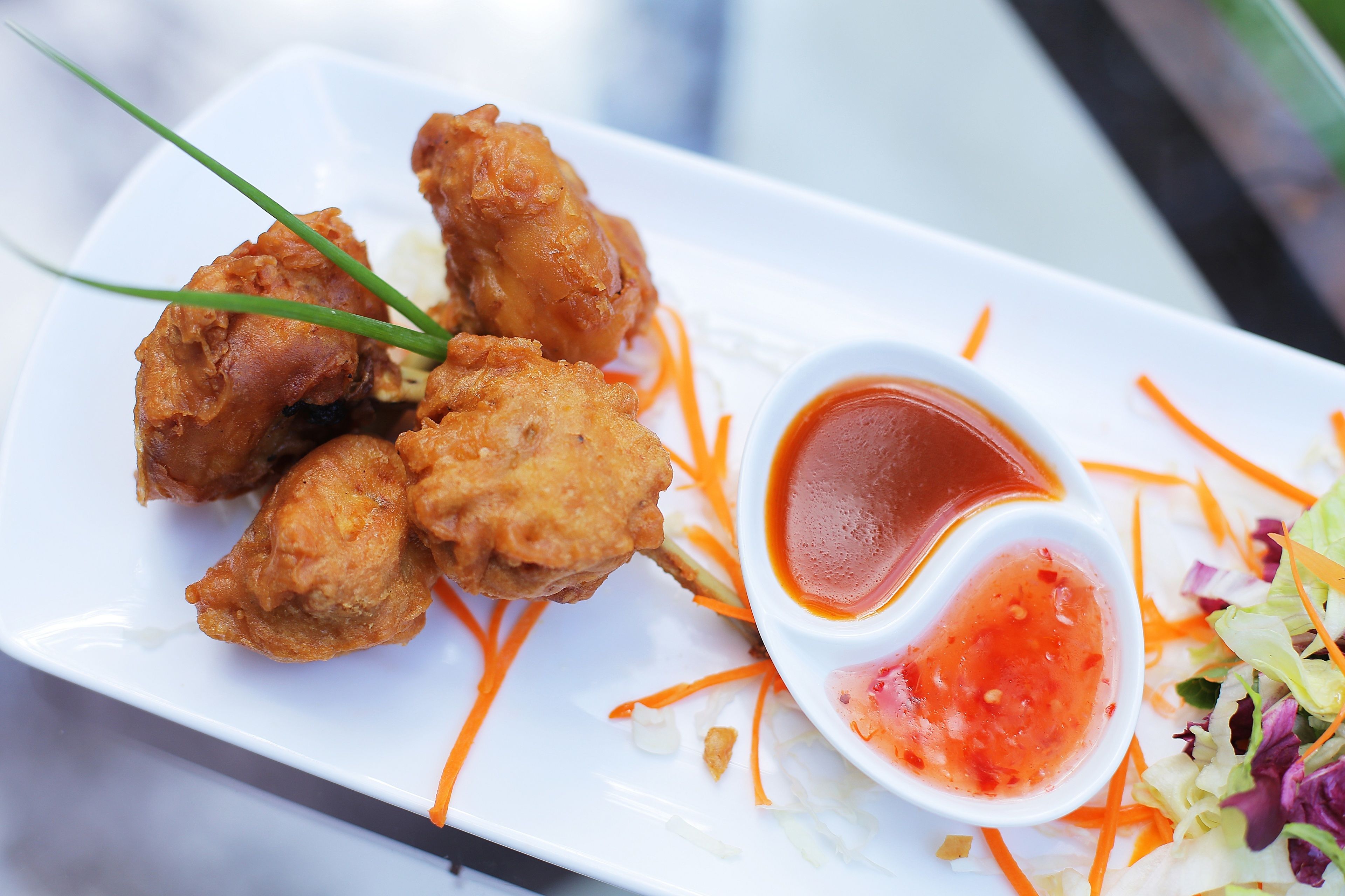 Une assiette de poulet frit, accompagnée d’une portion de carottes râpées et d’un petit bol de sauce rouge.