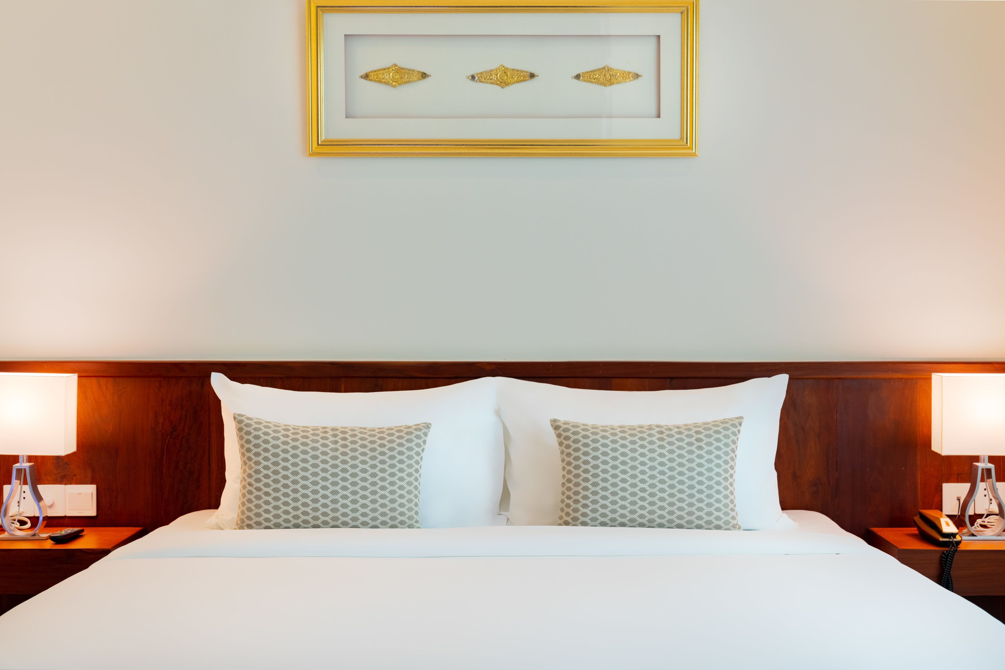 Una cama bien hecha con sábanas blancas y almohadas estampadas, flanqueada por dos mesitas de noche con lámparas y un teléfono.