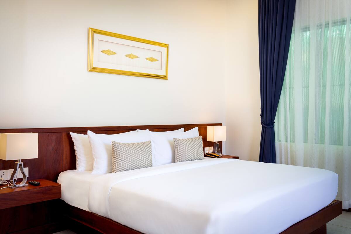 A neatly made bed with white linens, a wooden headboard, and two bedside tables with lamps.