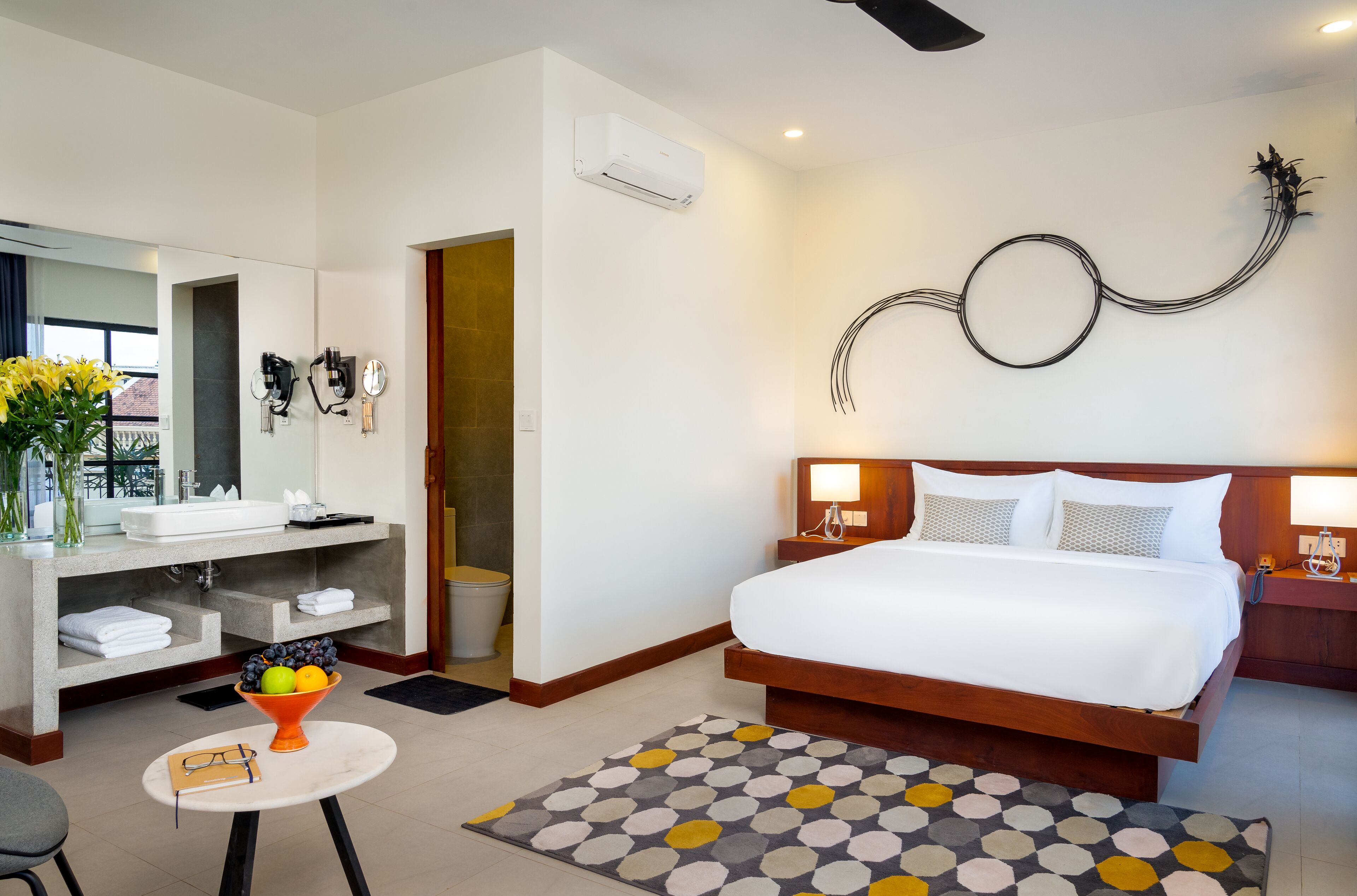 Quarto de hotel moderno com uma cama grande, banheiro com toucador e uma obra de arte original na parede.