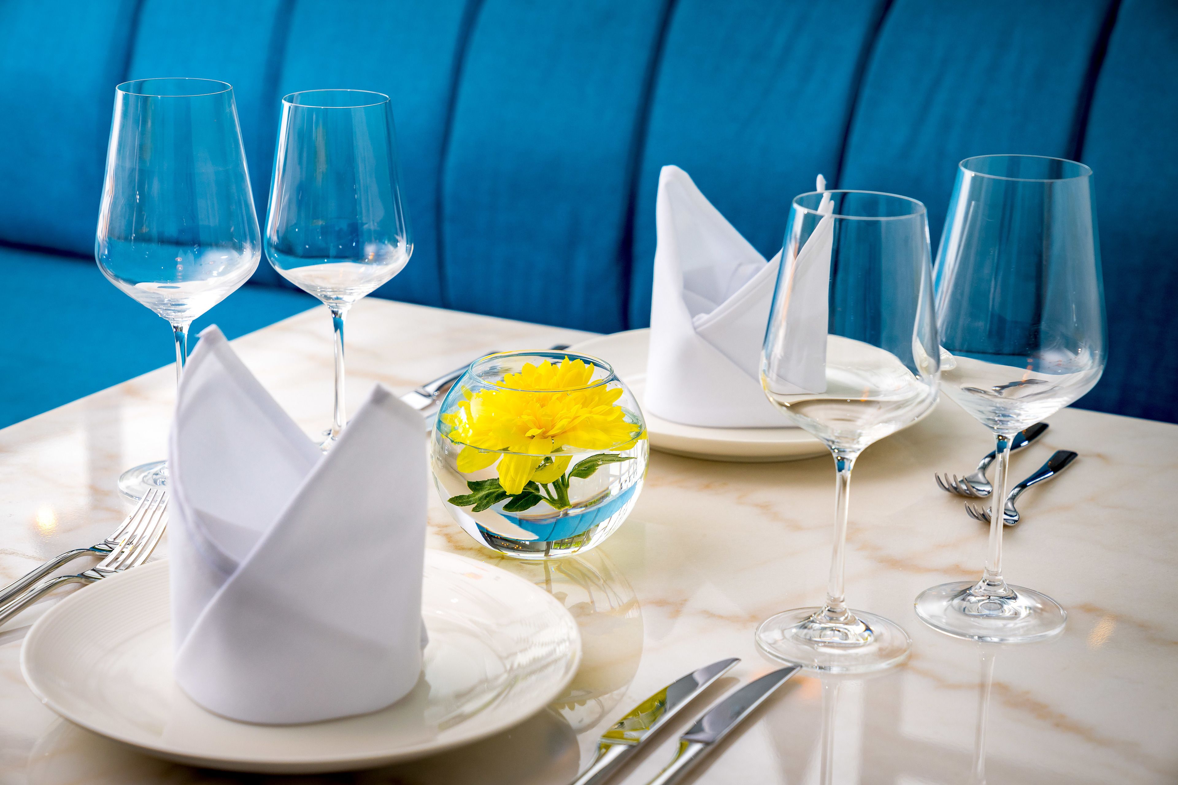 A table set with wine glasses, plates, and a glass bowl containing yellow flowers.