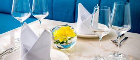 A table set with wine glasses, plates, and a glass bowl containing yellow flowers.