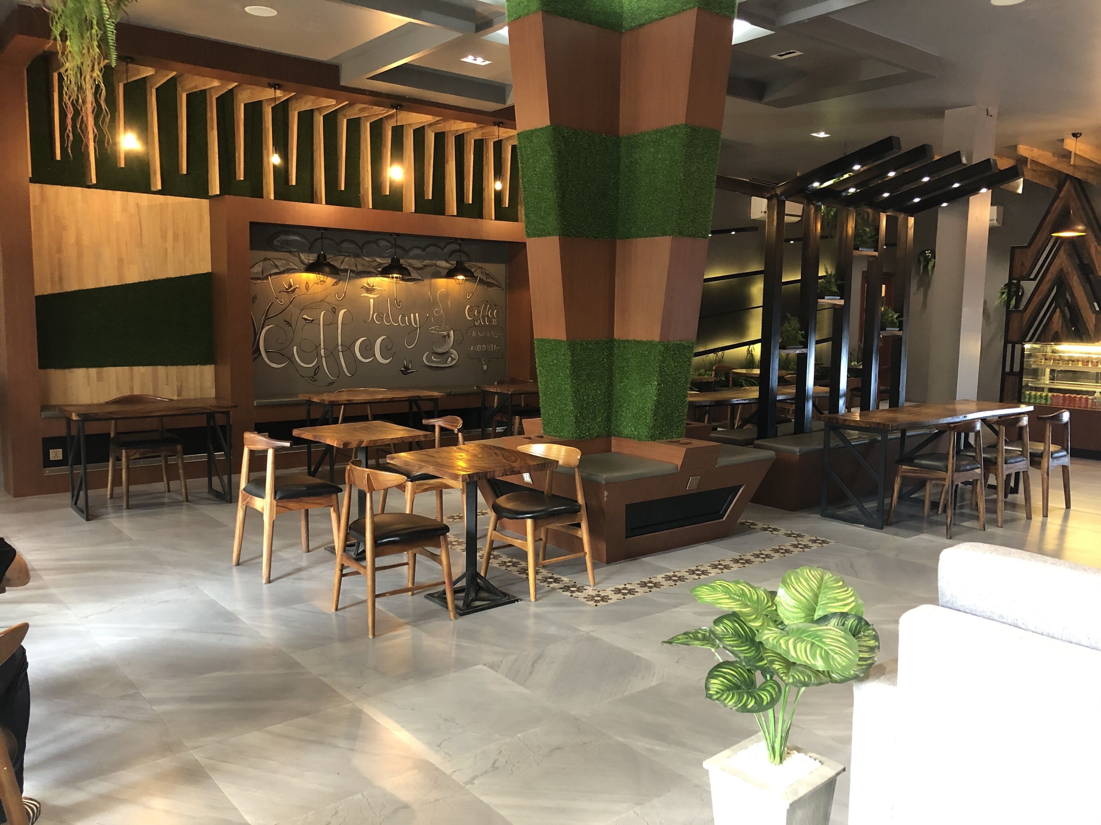 A modern cafe interior with wooden tables and chairs, a chalkboard menu, and green artificial grass accents.