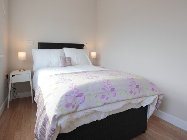 A neatly made bed with a floral bedspread, two bedside lamps, and a power outlet on the nightstand. - The Otton Suite (Dungannon)