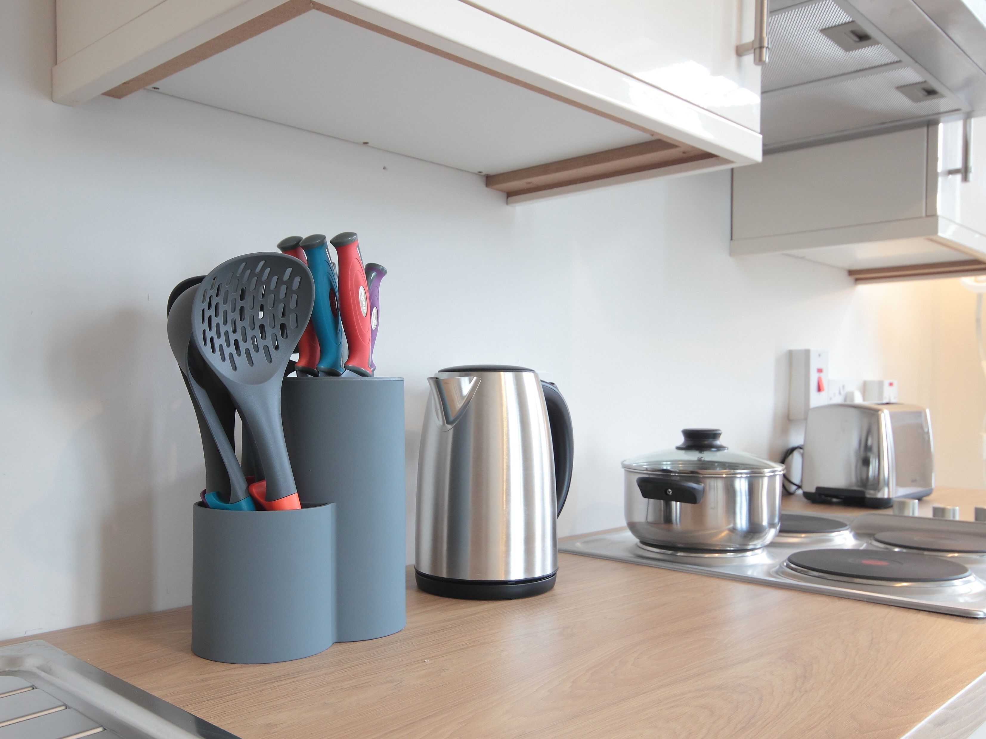 A kitchen with a wooden countertop, a kettle, a pot, and a set of colorful utensils in a holder.