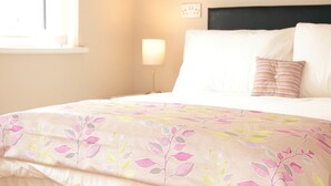 A neatly made bed with a floral-patterned bedspread, a bedside lamp, and a power outlet on the wall.