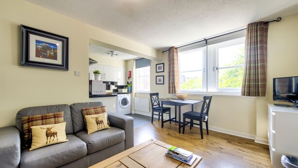 A living room with a grey sofa, a wooden coffee table, and a dining area with a table and chairs. - Stunning Studio Apartment Castle View (Edinburgh)