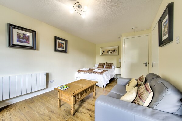 A room with a bed, a grey sofa, a wooden coffee table, and framed pictures on the walls. - Stunning Studio Apartment Castle View (Edinburgh)