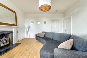 A living room with a grey sectional sofa, a fireplace, a floor lamp, and a large mirror on the wall. - Johnston Terrace Apartment (Edinburgh)