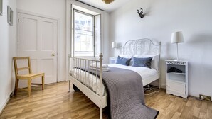 Een slaapkamer met een bed, een stoel, een nachtkastje en een raam.