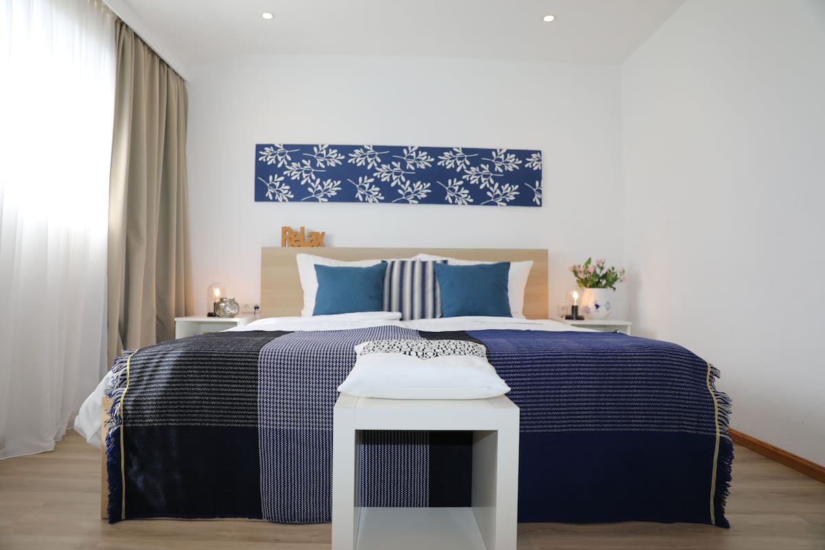 A modern bedroom with a large bed, a bedside table with a lamp, and a wall-mounted artwork.
