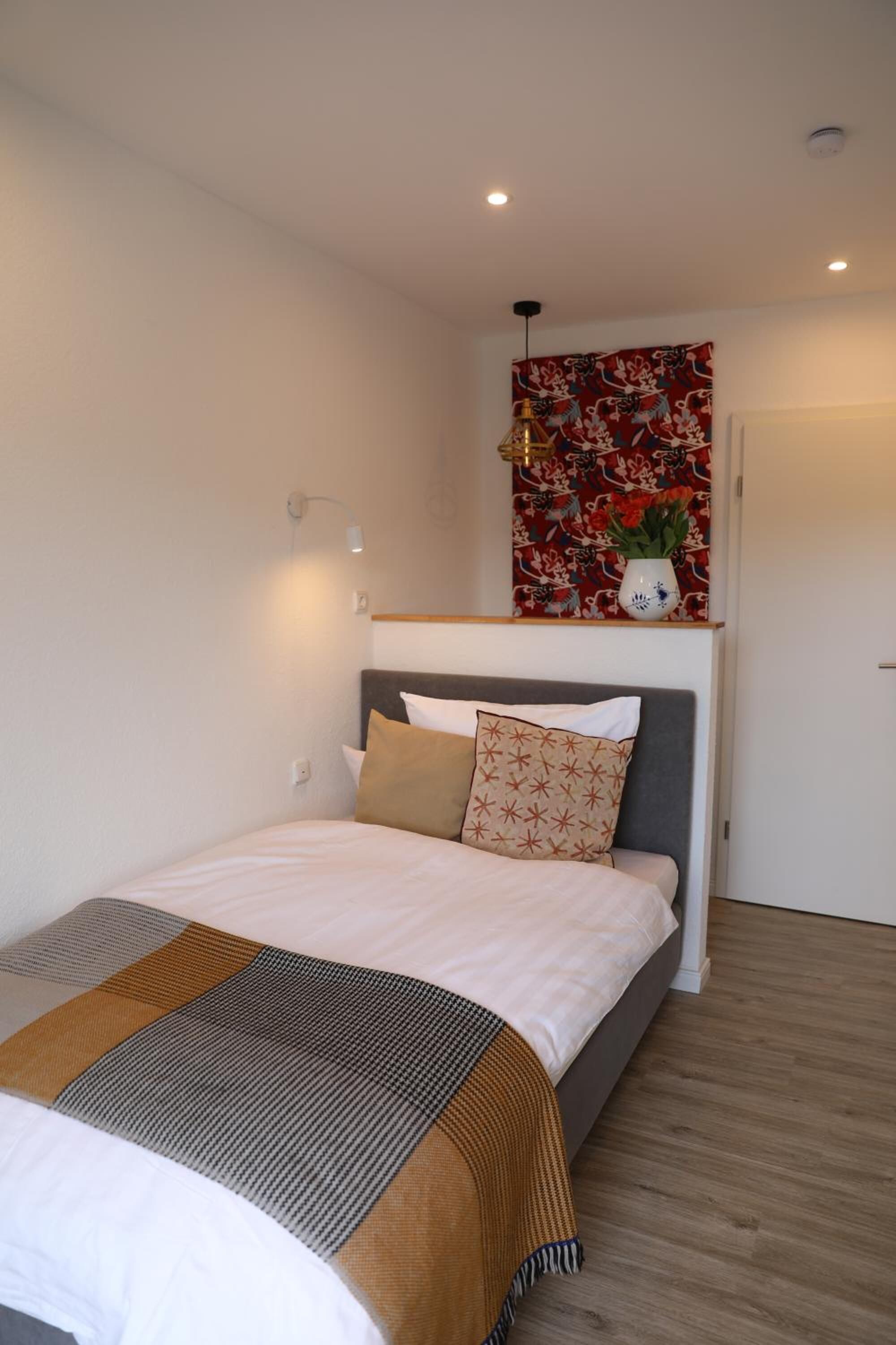 Ein modernes Schlafzimmer mit einem Bett, einem Kopfteil, einer Wandleuchte und einem floralen Kunstwerk über dem Bett.