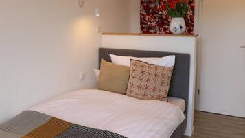 Ein modernes Schlafzimmer mit einem Bett, einem Kopfteil, einer Wandleuchte und einem floralen Kunstwerk über dem Bett.