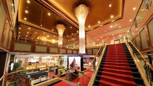 Un hall d’hôtel doté d’un escalier recouvert d’une moquette rouge, d’un bar et d’un espace salon avec des canapés verts et bleus.