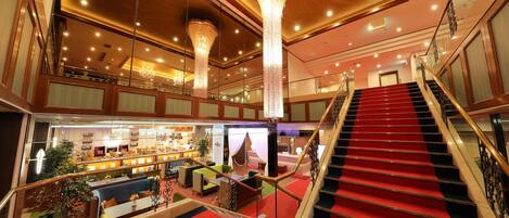 A hotel lobby with a red carpeted staircase, a bar area, and a seating area with green and blue sofas.