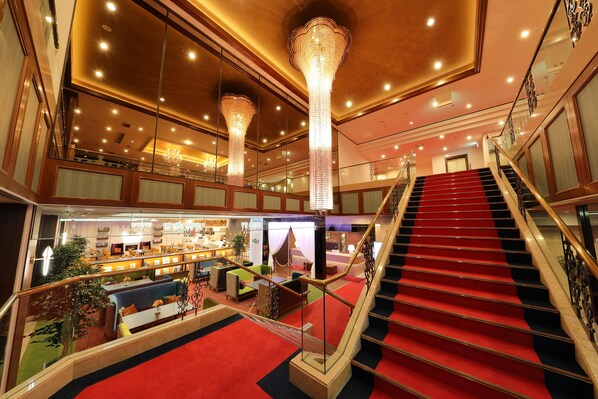 A hotel lobby with a red carpeted staircase, a bar area, and a seating area with green and blue sofas. - Garden Hotel Shiunkaku Higashimastuyama (Higashimatsuyama)