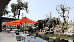 Une terrasse extérieure avec des tables et des chaises, un petit étang et une cascade.