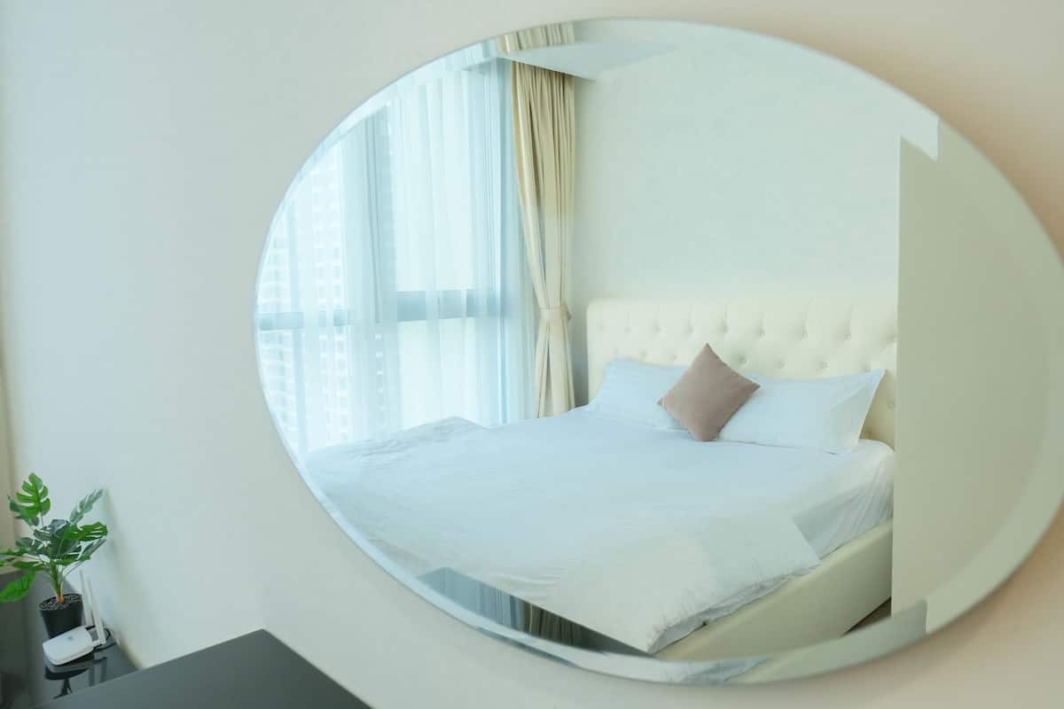 A bedroom with a large round mirror reflecting a bed with white bedding and a tufted headboard.