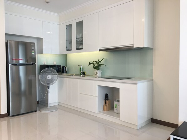 A modern kitchen with white cabinetry, a stainless steel refrigerator, a microwave, a toaster, a sink, a fan, and a potted plant. - Jack Hai Vinhome Apartment (Ho Chi Minh City)