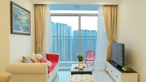 A modern living room with a sofa, ottoman, TV stand, and a large window with a city view. - Jack Hai Vinhome Apartment (Ho Chi Minh City)