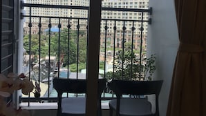 A balcony with a view of high-rise buildings, a potted plant, and two chairs. - Jack Hai Vinhome Apartment (Ho Chi Minh City)