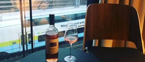 Una mesa con una botella y una copa de vino, una silla y una vista de un tren a través de una ventana.