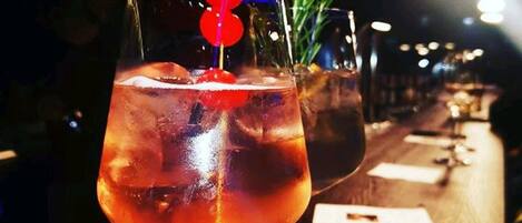 A bar setting with a glass of a reddish beverage, ice cubes, and a red garnish.
