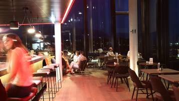 Un restaurante moderno con techos altos, ventanas amplias y una variedad de opciones de asientos, incluyendo taburetes de bar y mesas.