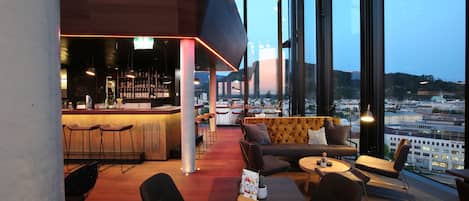 Un área de bar moderna con mostrador, asientos y vistas a la ciudad.