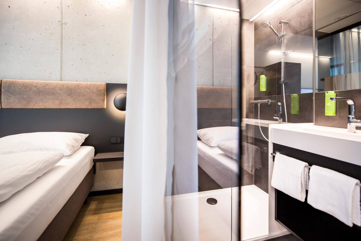 Ein modernes Hotelzimmer mit einem großen Spiegel, einer Dusche und einem Bett.