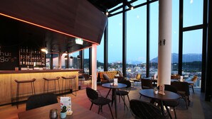 Zona de bar moderna con techo alto y amplios ventanales que ofrecen vista a la ciudad.