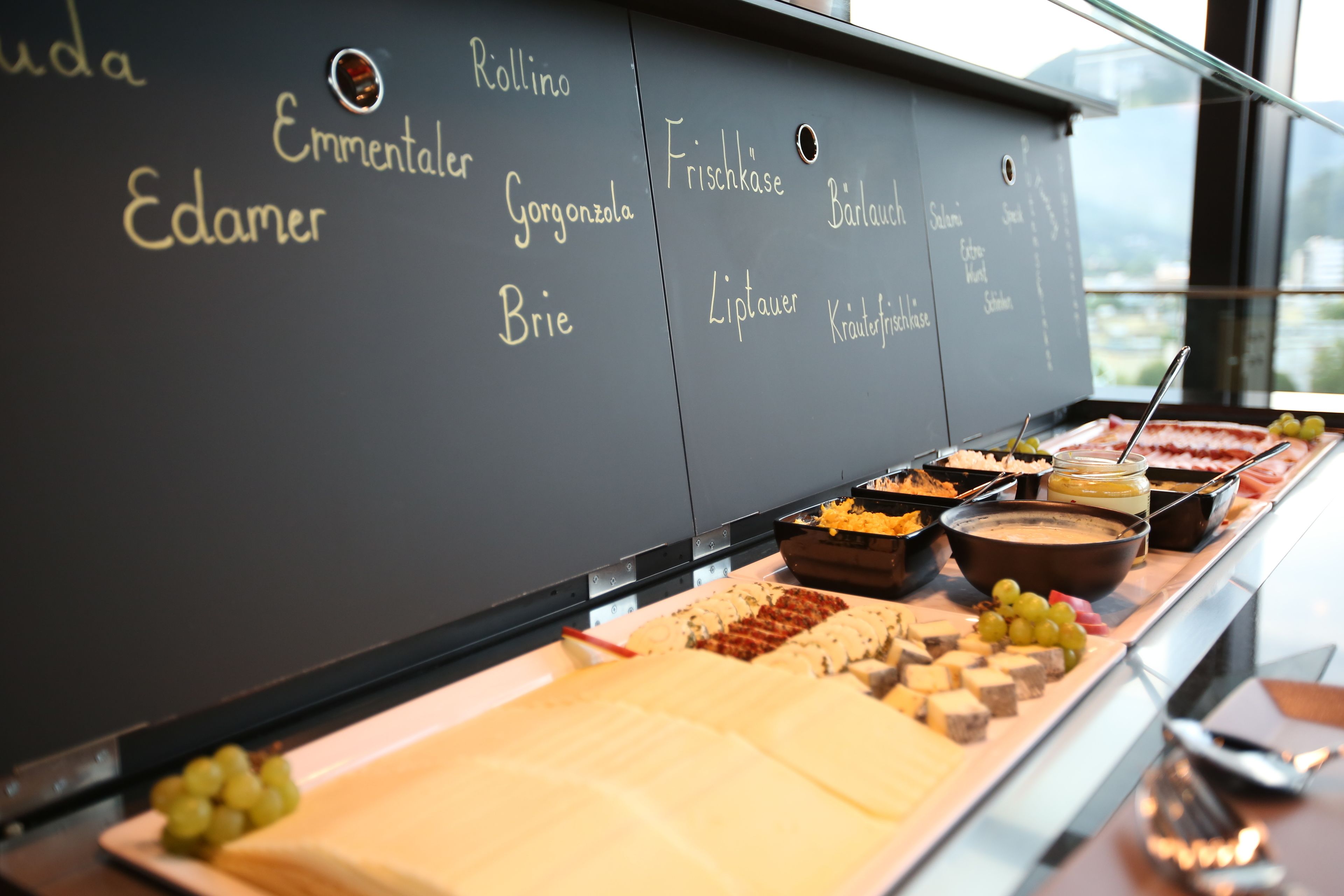 A buffet with various cheeses and fruits, and a chalkboard listing food items.