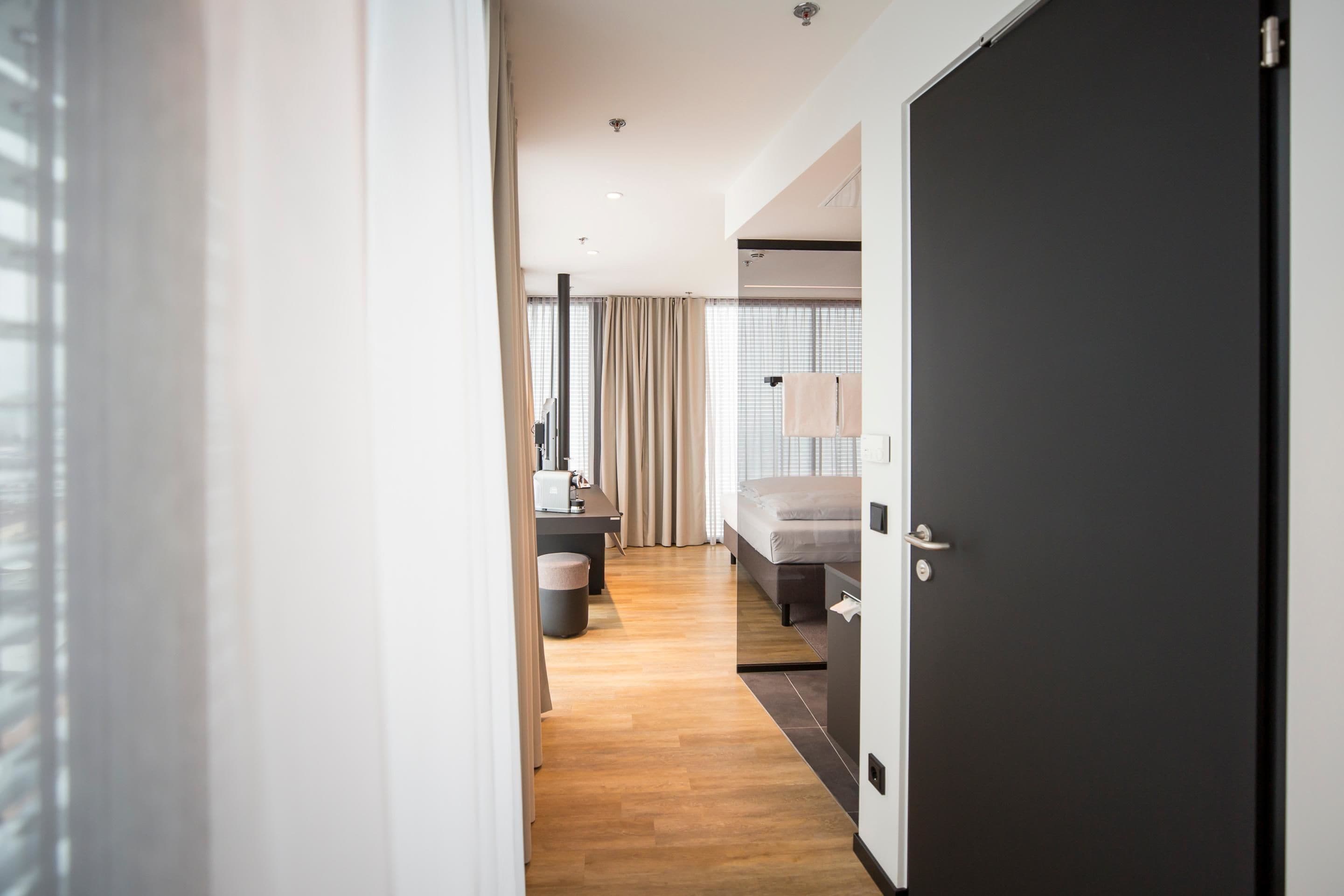 Ein modernes Hotelzimmer mit Holzboden, einem Bett, einem Schreibtisch und einem Stuhl.