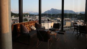 Un salón moderno con sofá y sillones, amplias ventanas con vista a la ciudad y a las montañas.