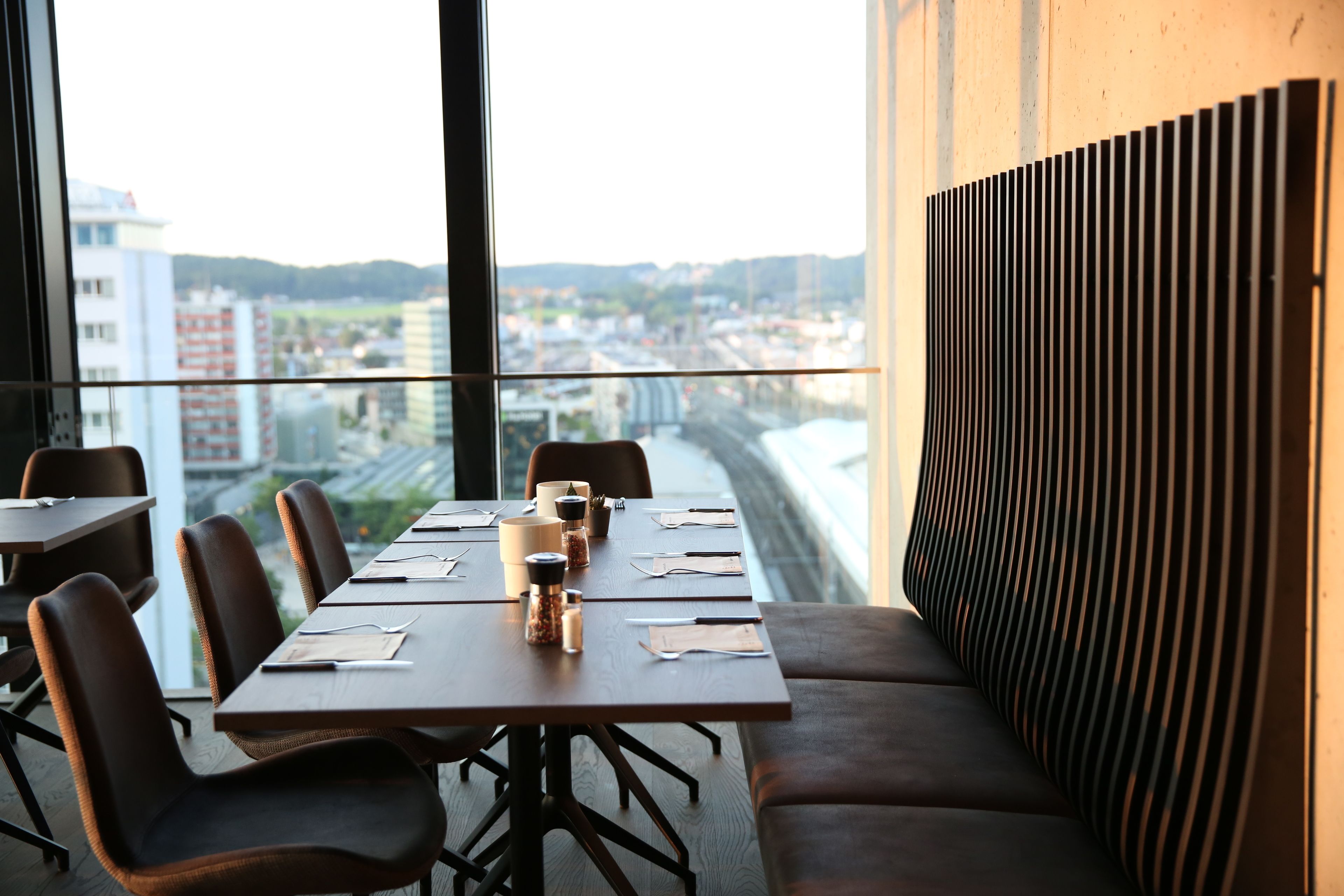 A conference room with a long table, chairs, and a view of a cityscape through large windows.