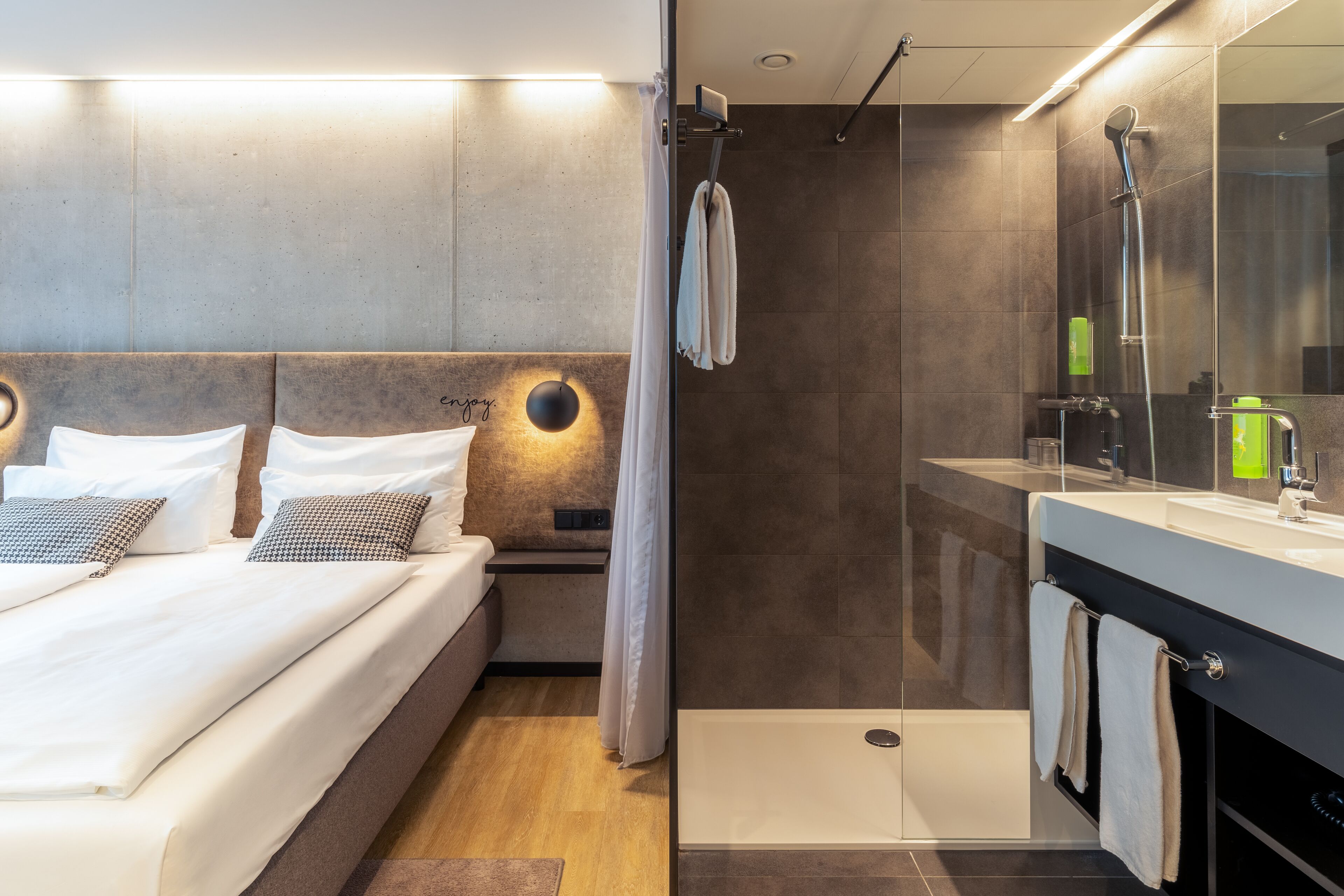 A modern hotel room with a bed, bedside table, and a shower area.