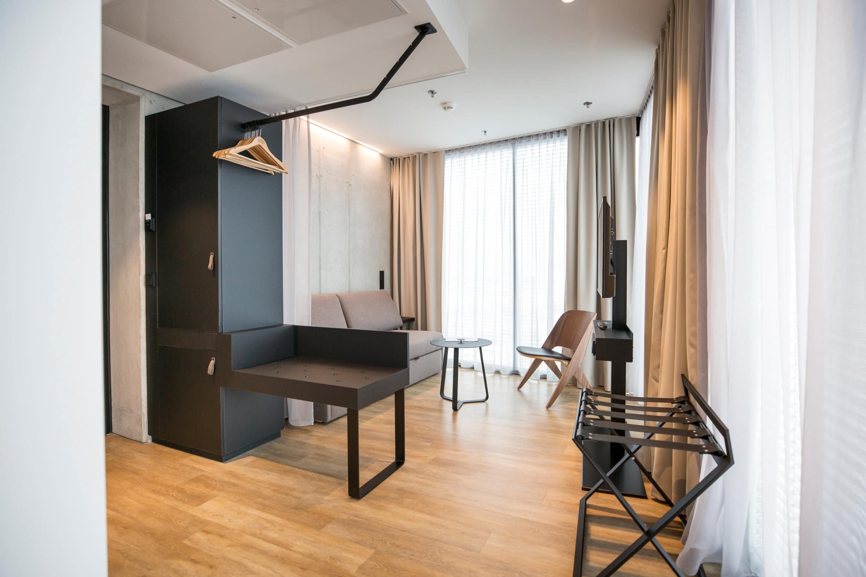 A modern living room with a sofa, a small table, a TV, and a hanging clothes rack.
