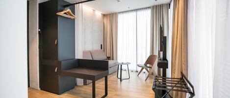 A modern living room with a sofa, a small table, a TV, and a hanging clothes rack.