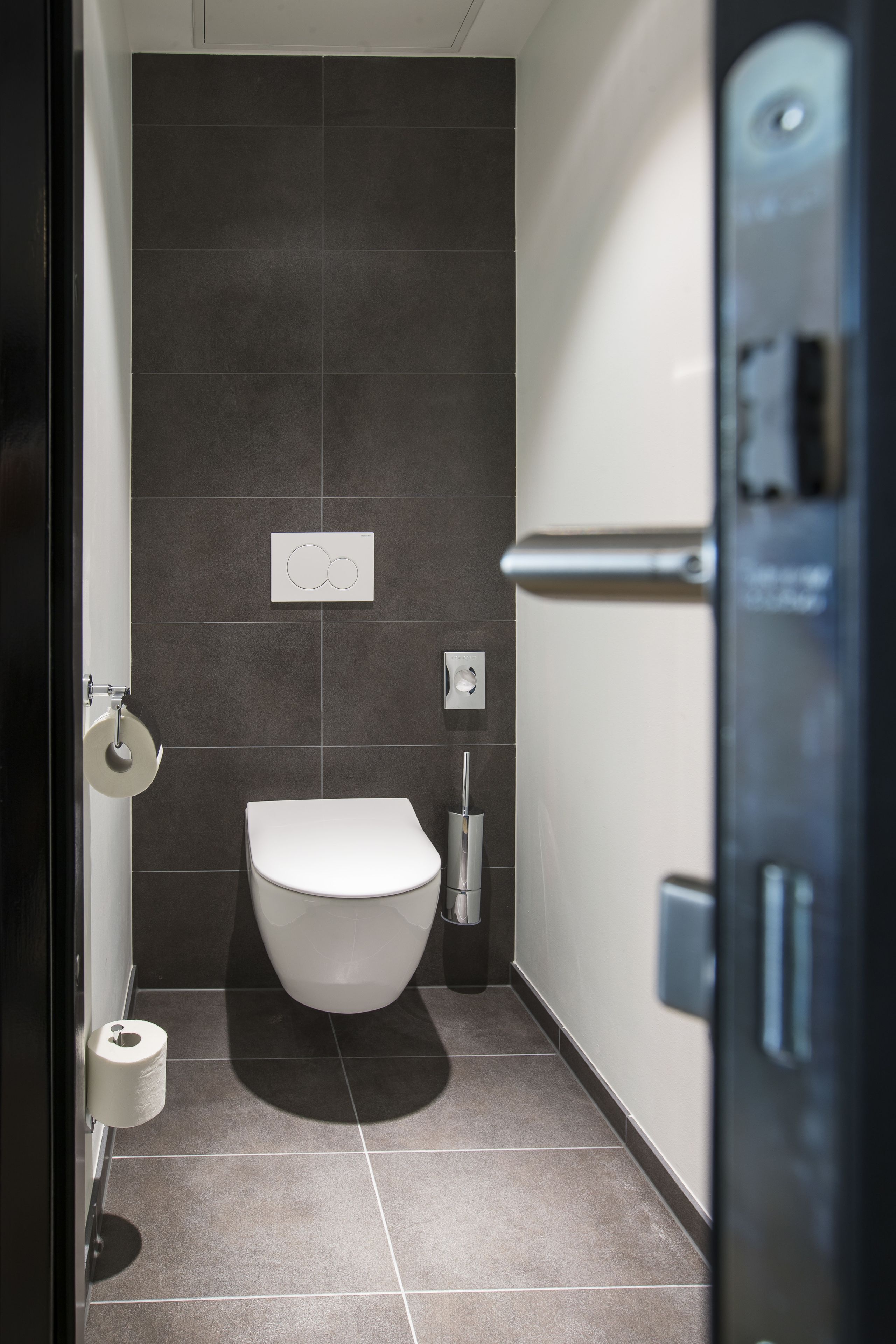 Een moderne badkamer met toilet, donkere tegels en een handdroger.