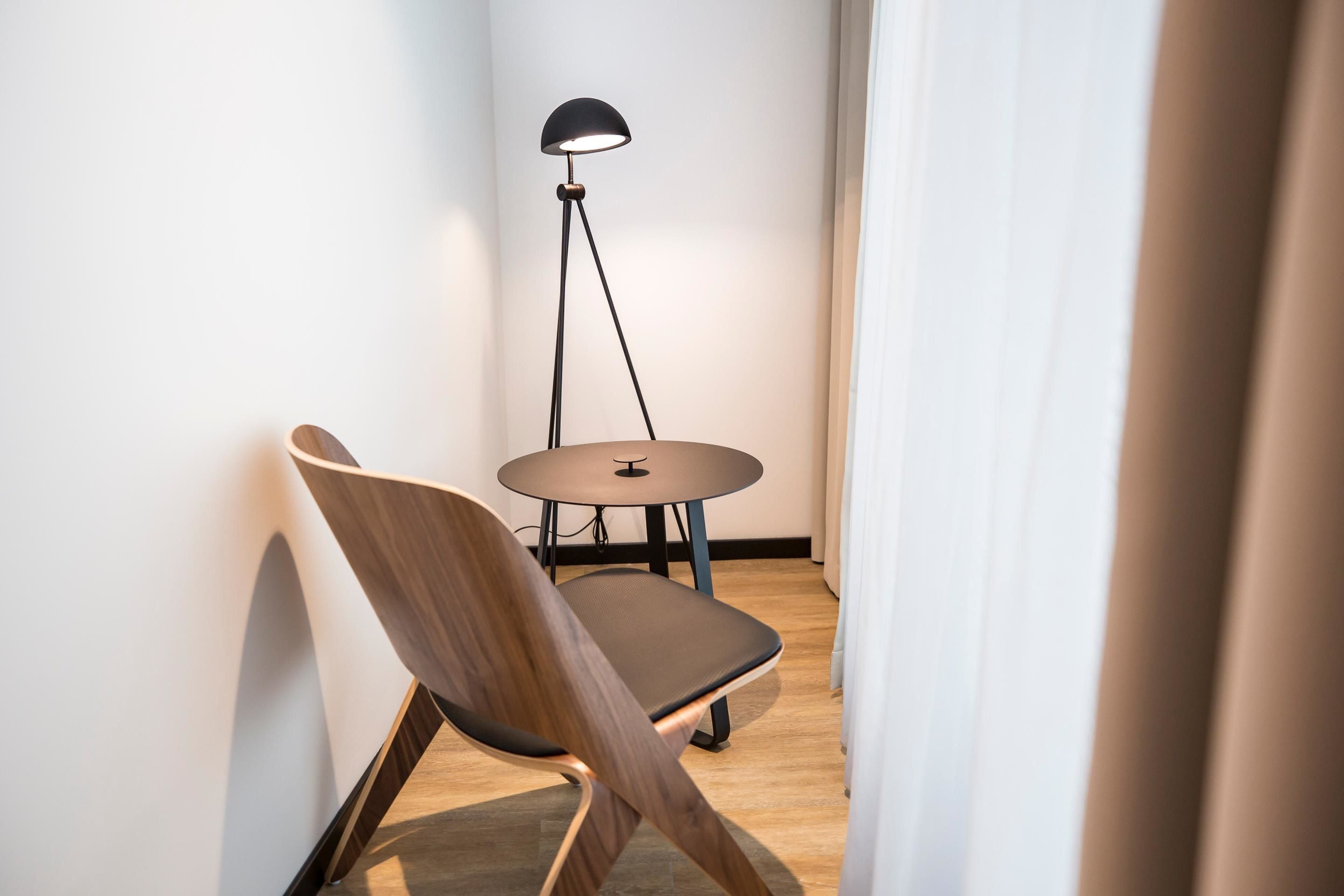 A modern room with a wooden chair, a small round table, and a floor lamp.