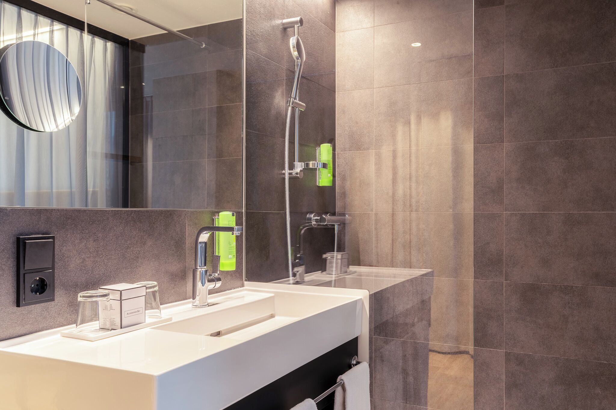 A modern bathroom with a large mirror, a white sink, a shower, and a towel rack.