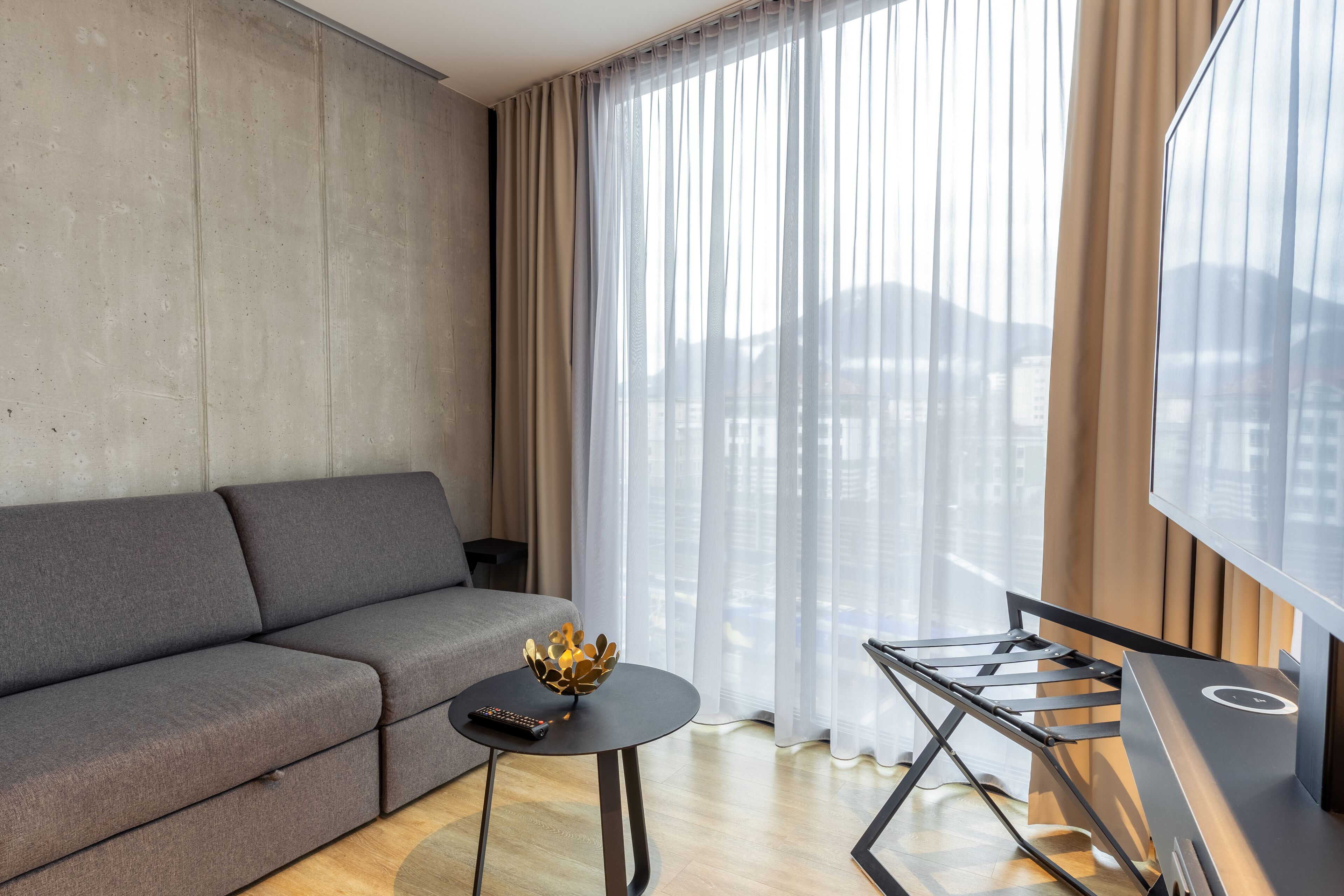 Una sala de estar moderna con un sofá gris, una mesita redonda con un objeto decorativo y un mueble de televisión con una pantalla plana.