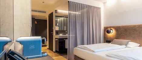 A hotel room with a bed, a desk with a telephone, a mirror, and a bathroom visible through a door.