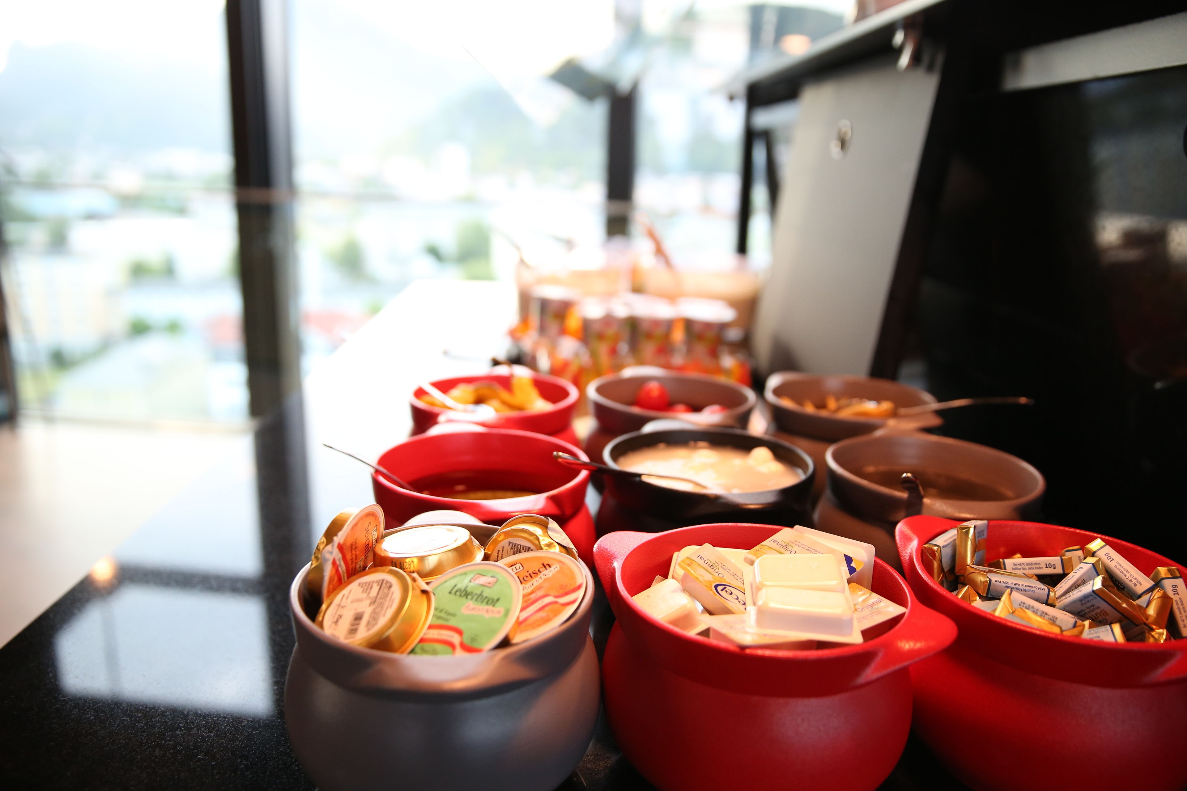 Une table de buffet avec différents plats présentés dans des bols rouges et gris.