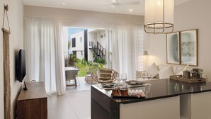 A modern kitchen with a central island, a dining area with a chair, and a view of a staircase leading to a balcony. - O'Biches by Horizon Holidays (Trou aux Biches)